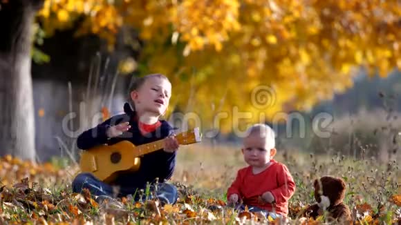 秋天公园里逗乐的孩子用吉他唱歌给小弟弟的画像视频的预览图