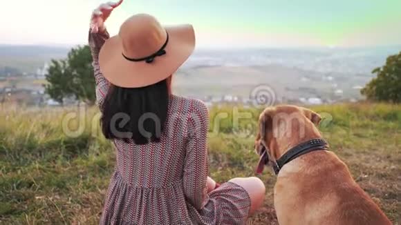 带帽子的可爱女孩的后景和她可爱的狗坐在草地上视频的预览图