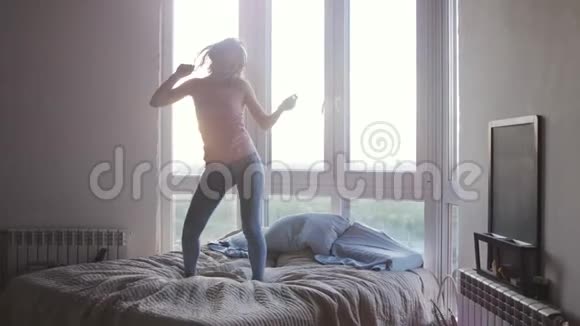 在美丽的日出期间年轻漂亮开朗的女人在豪华公寓的床上跳着舞有镜头闪光的效果视频的预览图