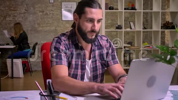 有着黑胡子的白种人很享受他一边看着电脑一边打字一边在工作场所玩得很开心视频的预览图