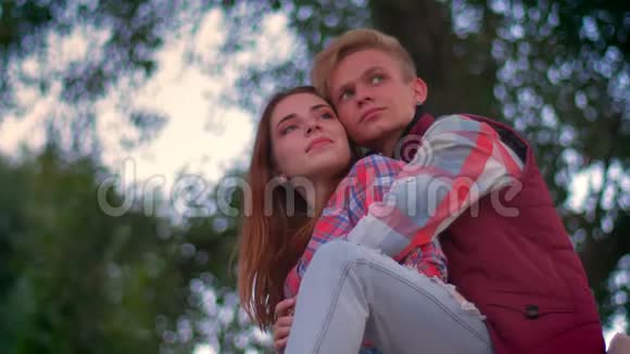 男人坐在篱笆上而他的女朋友站在他身边被抱着看着前方绿树成荫视频的预览图