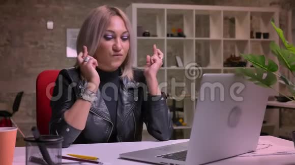 集中精力可爱的白种人金发女人正在交叉手指而独自坐在办公室看着视频的预览图