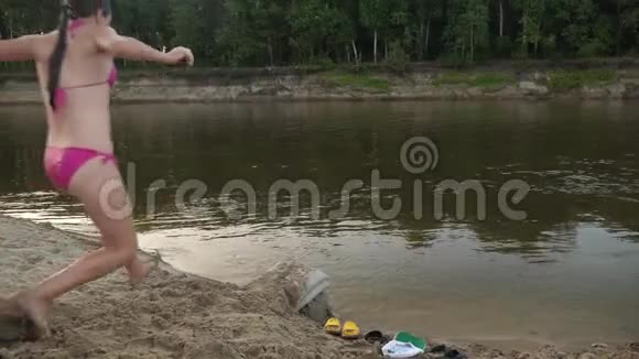 穿着泳衣的苗条女孩沿着海滩跑跳进水里溅到不同的方向慢慢视频的预览图