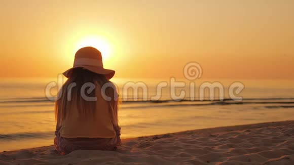 一个孩子坐在沙滩上看着大海上的夕阳视频的预览图