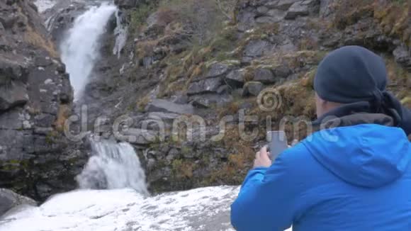 一个男人在山上拍摄一个美丽的瀑布在智能手机上过着活跃有趣的生活视频的预览图