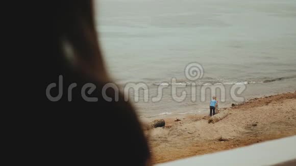 独自一人的女人早上在阳台上喝咖啡或茶有蓝色的海景孩子们在海边玩耍视频的预览图