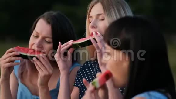 三个年轻迷人的女朋友在日落时穿着蓝色连衣裙吃西瓜和微笑视频的预览图