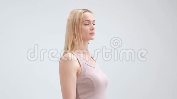 漂亮优雅的金发女人穿着米色连衣裙在白色背景上摆姿势微笑视频的预览图