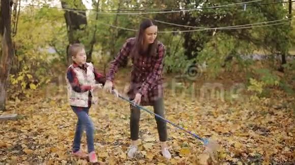 一个小女孩和她妈妈用耙子在院子里做黄叶清理秋叶视频的预览图