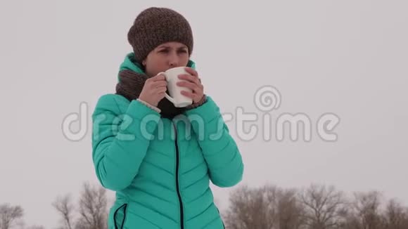 女孩在冬天的公园里在寒冷的新鲜空气中喝着杯子里的热咖啡视频的预览图
