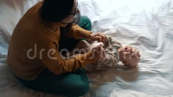 女人笑着和她的小婴儿在白色的床上玩耍母亲和孩子视频的预览图