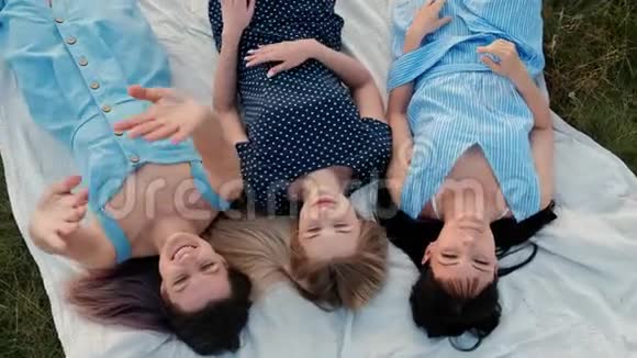 三个年轻迷人的女人躺在格子布上看着天空笑点起来跳舞休息女朋友视频的预览图