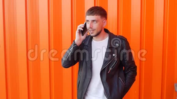 年轻的白种人穿着黑色夹克在电话里有感情地交谈在橙色的衣服上玩得很开心视频的预览图