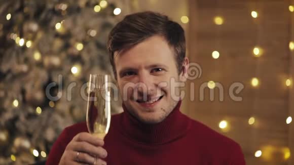 有魅力的男人带着一杯香槟看着圣诞树背景上的相机他举起杯子慢慢视频的预览图