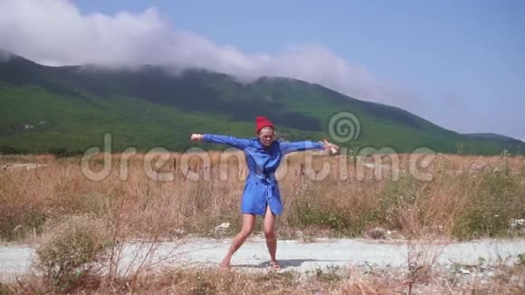 性感的女孩在山上的一条路上跳舞她穿着蓝色的外套戴着红色的帽子手里拿着一个木棍视频的预览图