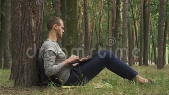森林里的一棵树下坐着一台笔记本电脑的年轻人视频的预览图