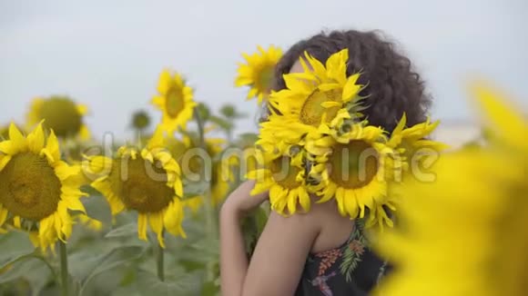 一个美丽的卷曲女孩站在向日葵田上的花束的肖像明亮的黄色视频的预览图