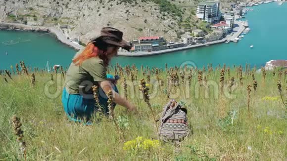 美丽的红发女孩戴着牛仔帽穿过海边的群山视频的预览图