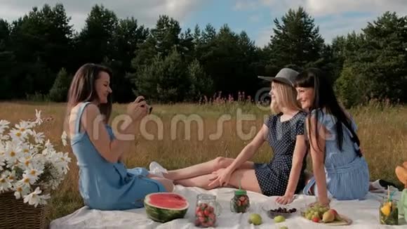 三个年轻漂亮的女孩在野餐摄影师在两个模特的无镜相机上拍照模型视频的预览图