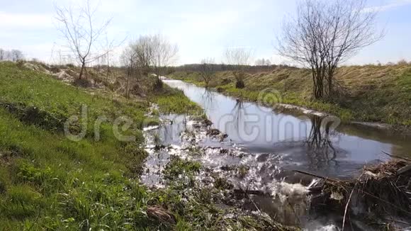 春季绿田与垃圾坝之间的河流水流视频的预览图
