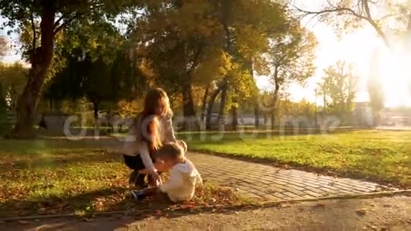 妈妈和孩子一起在秋日公园散步婴儿坐在草坪上母亲从草地上抚养婴儿视频的预览图