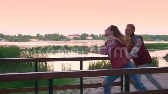 快速奔跑的女孩靠近她的男朋友牵着他的手用迷人的微笑桥景和看着他视频的预览图