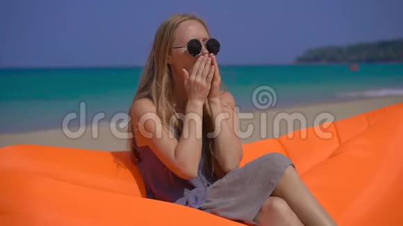 一名年轻女子坐在热带海滩上的充气沙发上咳嗽时的超慢镜头旅行疾病视频的预览图