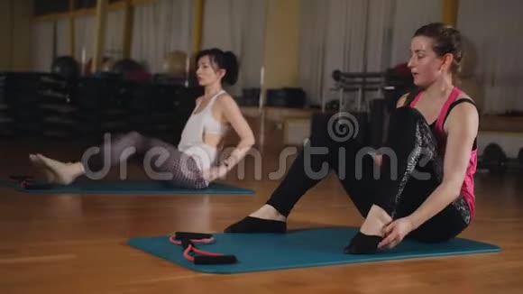 女人在健身房做普拉提练习女孩坐在地板上的分裂和伸展双手到脚视频的预览图