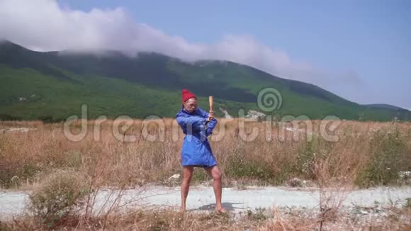 性感的女孩在山上的一条路上跳舞她穿着蓝色的外套戴着红色的帽子手里拿着一个木棍视频的预览图