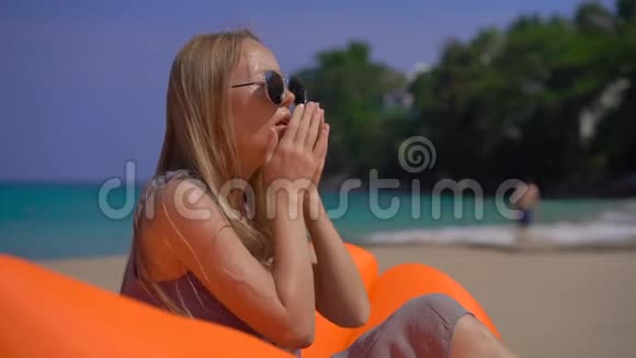 一名年轻女子坐在热带海滩上的充气沙发上咳嗽时的超慢镜头旅行疾病视频的预览图