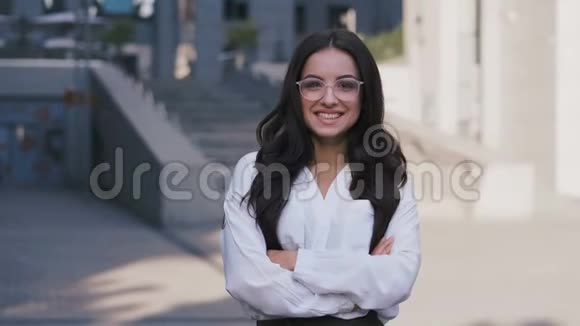 年轻的成功女商人戴着眼镜站在现代办公楼附近看着相机和视频的预览图