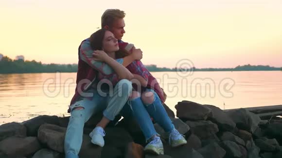 爱的美丽的一对夫妇坐在石头上牵着手河流的背景和美丽的天空大自然视频的预览图