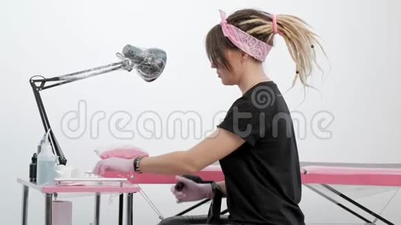一位迷人的女纹身大师的肖像时尚女孩与可怕的在白色和粉红色的工作室背景视频的预览图