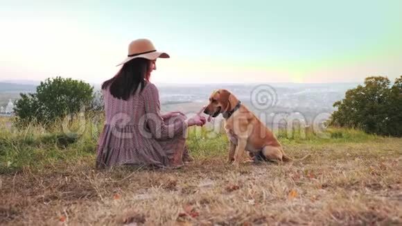 带帽子的可爱女孩的后景和她可爱的狗坐在草地上视频的预览图