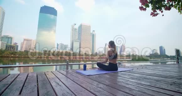 健身妇女坐在健身地毯上坐在城市公园里对着高楼大厦沉思她高兴地闭上眼睛视频的预览图