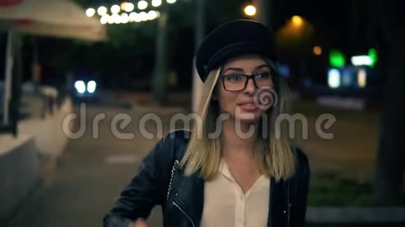 美丽的金发女人在夜间走在城市街道上时尚女性戴黑色帽子视频的预览图