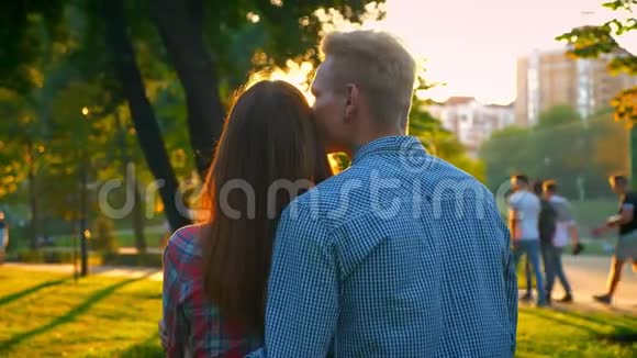 从后面射击可爱的白种人夫妇抱在一起站在阳光下向前看公园视频的预览图