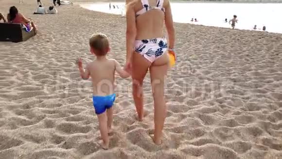 年轻母亲手牵着孩子在沙滩上散步的4K视频幼儿男孩在海滩上与视频的预览图