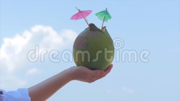 年轻的双手女人在热带海滩上的美丽的云彩背景中抱着椰子暑假的概念视频的预览图