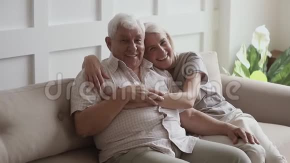 幸福的老夫妇坐在家里的沙发上画像视频的预览图