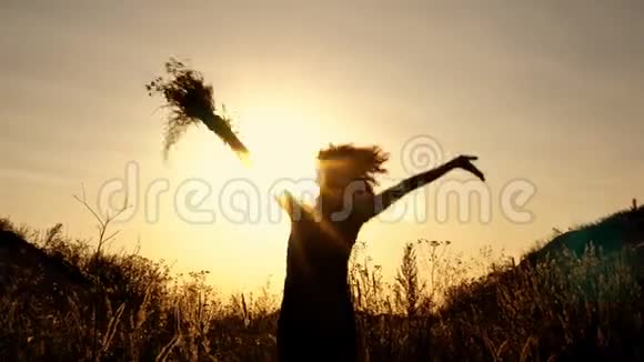 一个女孩在灿烂的夕阳背景下的黑色剪影她跳起来在花丛中挥动双手视频的预览图