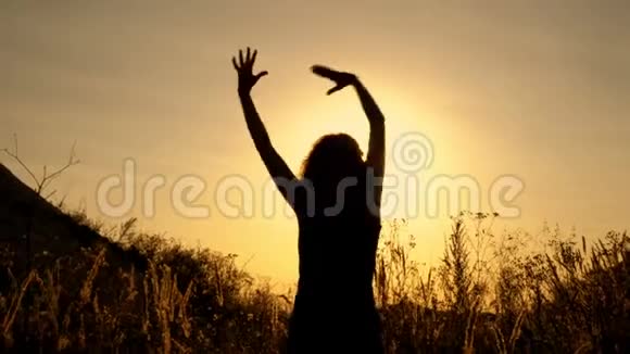阳光明媚的日落背景下的女孩站在田野的花丛中手挥手视频的预览图