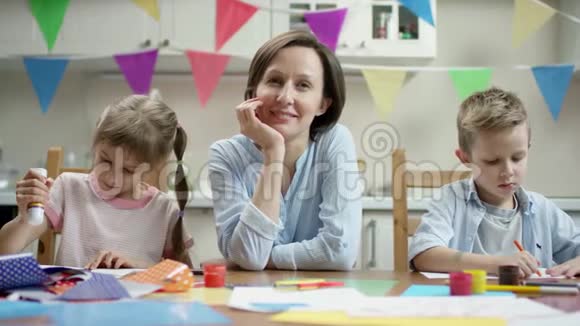 母亲和孩子们坐在一起一边制作节日工艺品一边微笑视频的预览图