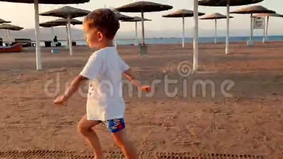 日落时分快乐快乐的男孩在海滩上奔跑的4镜头视频的预览图
