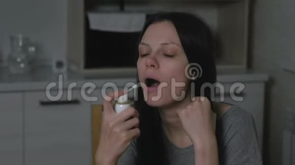 生病的年轻女人晚上在厨房里用喉喷雾剂在家治疗感冒视频的预览图