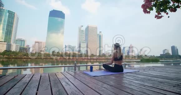 女人坐在健身地毯上在梅格波利斯市中心的高楼上沉思她闭上眼睛视频的预览图