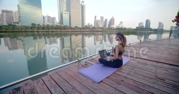 她喜欢在城市公园做自由职业户外工作她坐在健身地毯上在笔记本电脑上打字视频的预览图