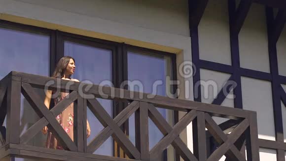 女人走在阳台上享受生活弯曲微笑快乐夏日生活无忧无虑视频的预览图