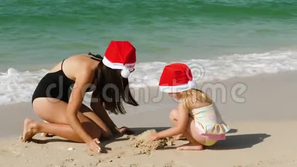 一个孩子和妈妈在海滩上戴着圣诞老人的帽子视频的预览图