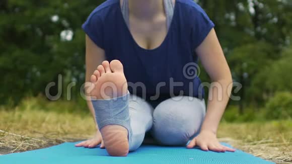 年轻女子在公园里练习腿部伸展弯下腰看镜头户外视频的预览图